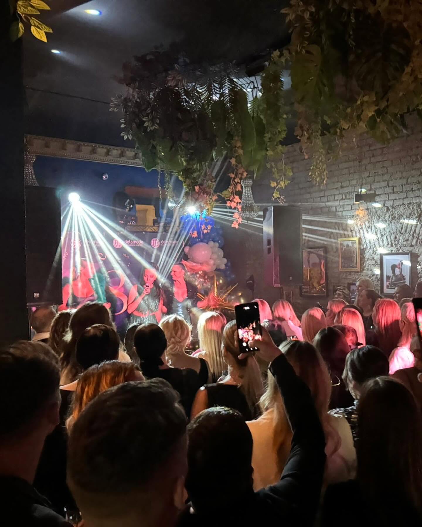 Renginio publika prie scenos su ryškiu dekoratyviniu apšvietimu